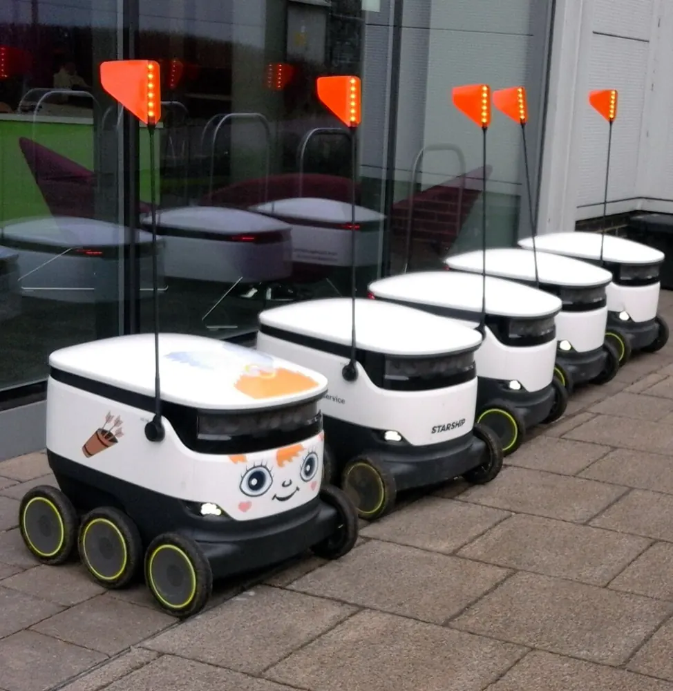 A row of five identical delivery robots parked on a pavement